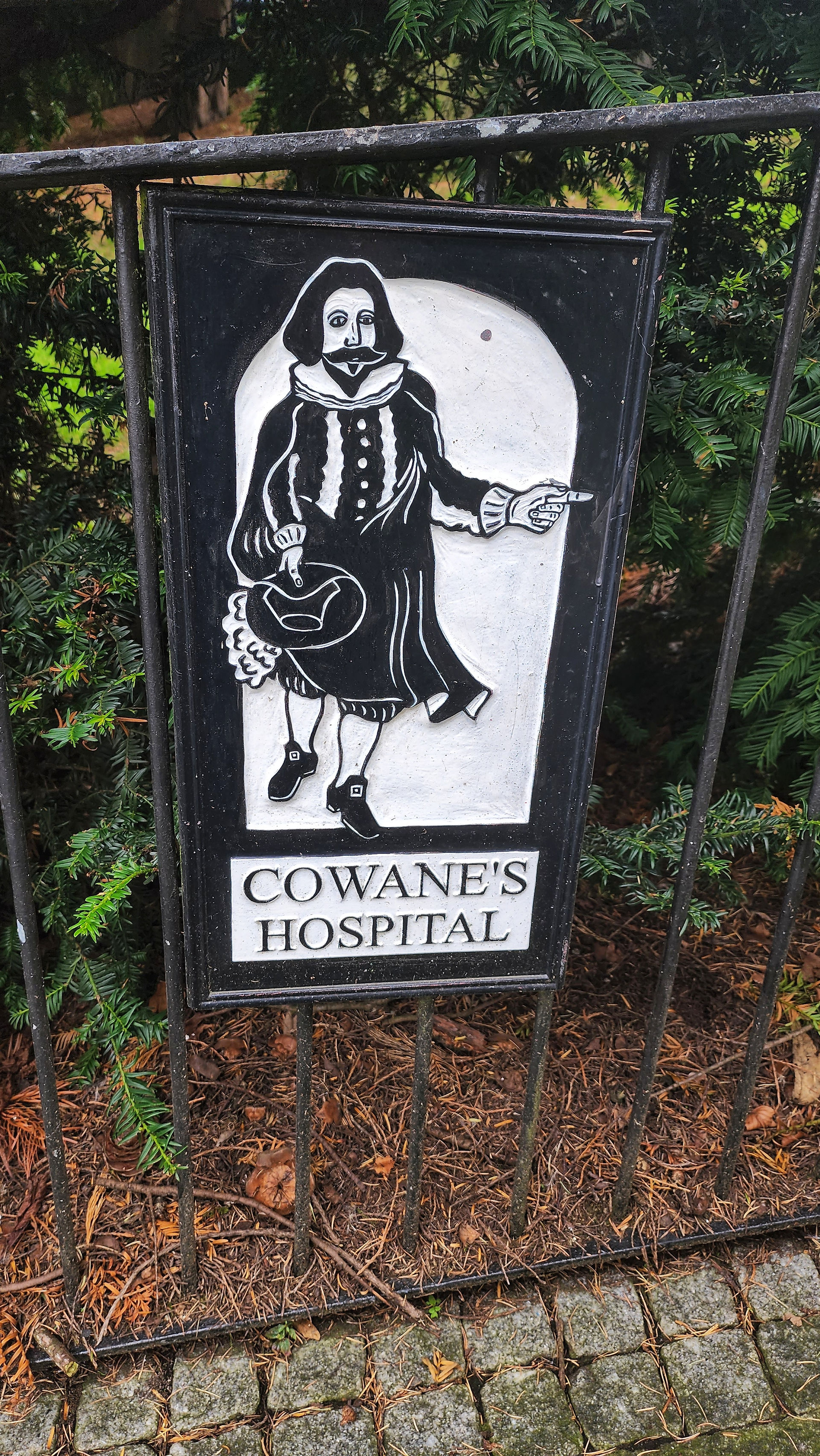 A black and white sign, showing a man in historic dress pointing the way to Cowane's Hospital