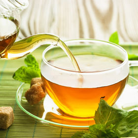 Pouring tea from glass teapot into clear cup with mint leaves background