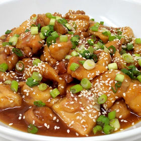 Delicious sesame chicken with green onions in white bowl, ready to eat.