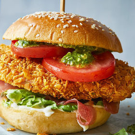 Delicious crunchy chicken burger with tomato, salad, and pesto on a bun