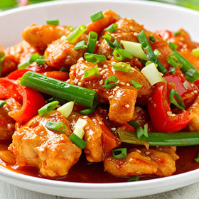 Chicken dish in white bowl with red peppers and green onions