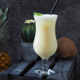 Pina colada cocktail with mint, pineapple, and coconut near cactus background