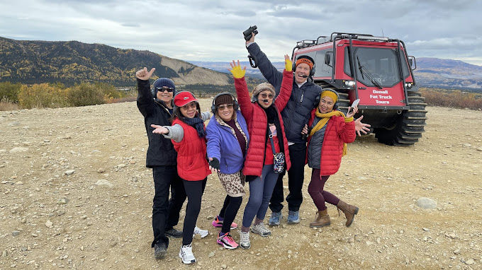 Happy group of visitors posing in front of a red Denali Fat Truck during a small group Alaska backcountry tour
