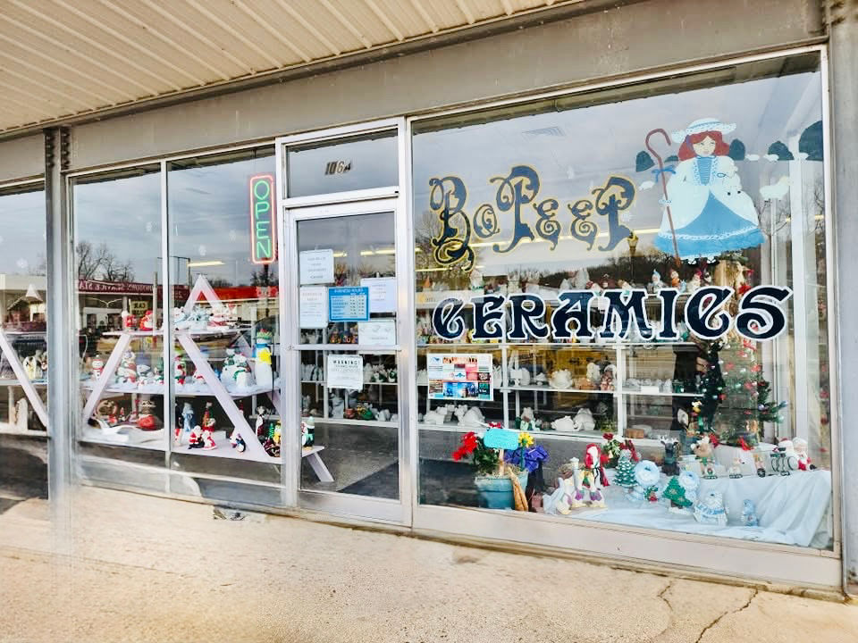 Storefront of "Bo Peep Ceramics" with a festive display of ceramic figurines. "Open" sign is visible. Bright and inviting atmosphere.