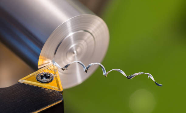 A carbide insert cutting a metal rod on a lathe machine, with precision chips forming as the tool operates.