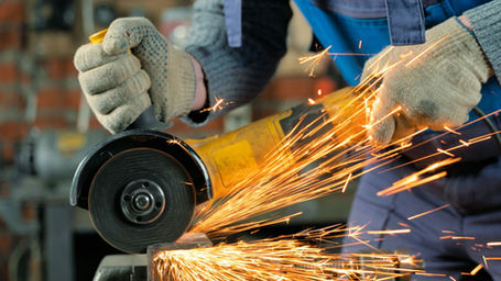 A worker wearing safety gloves using an angle grinder, producing bright sparks.