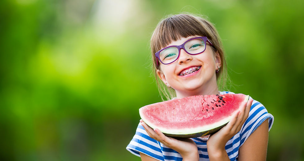 Young girl with braces holding a slice of watermelon and smiling outdoors.