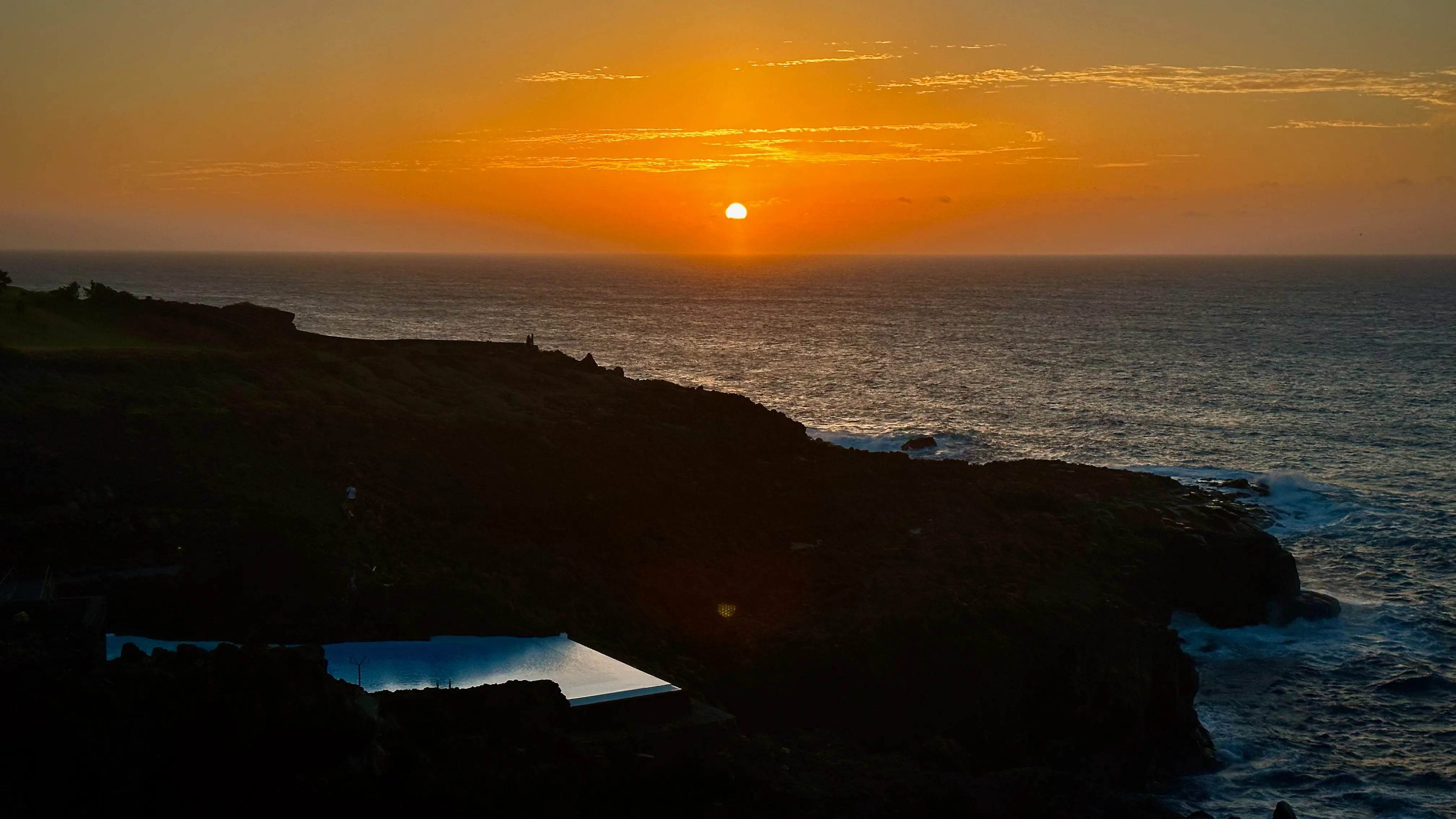Złoty zachód słońca nad oceanem na północnym wybrzeżu Teneryfy, z ciemnymi klifami i naturalnym basenem u stóp skał.