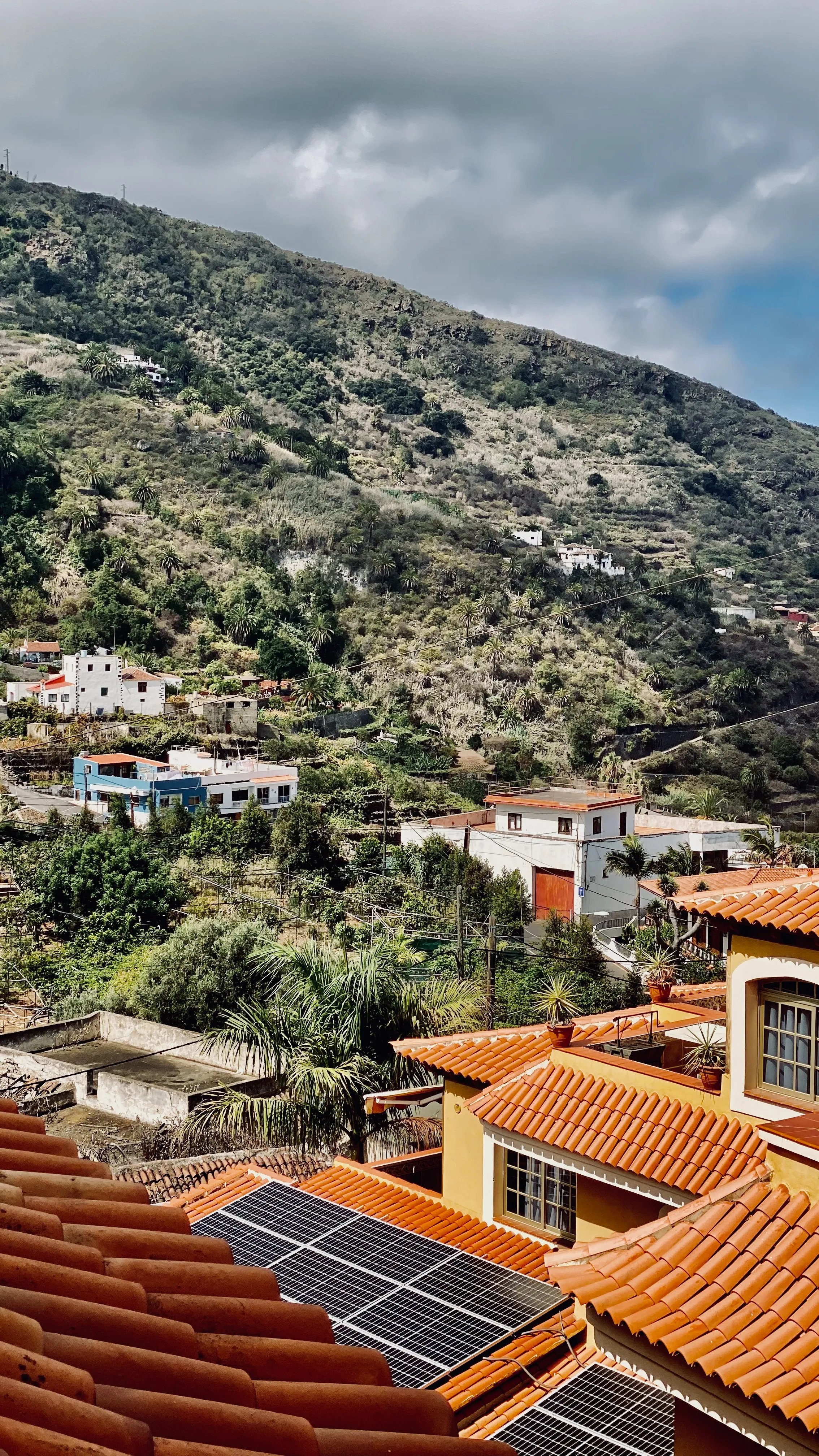 Widok z dachu na zieloną dolinę północnej Teneryfy – pomarańczowe dachówki, panele słoneczne i rozsiane po zboczach kolorowe domy.