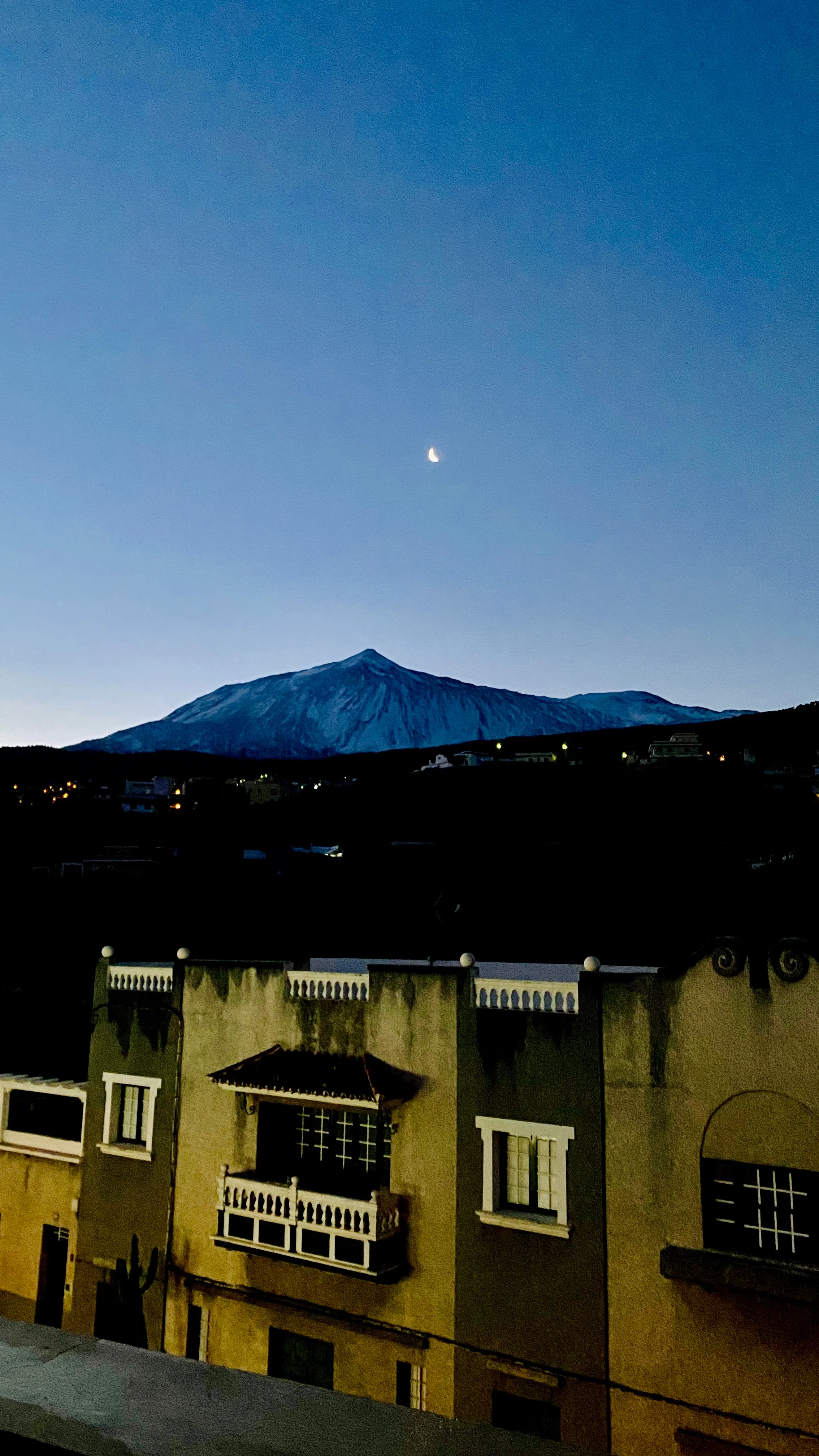 Teide o świcie z wiszącym nad szczytem księżycem, ponad fasadami domów – spokojny poranek na północnej Teneryfie.