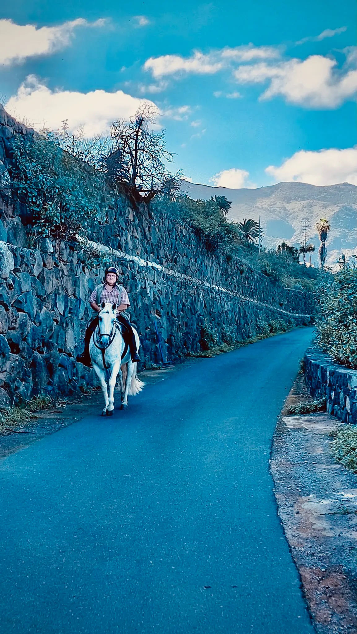 Tłum ludzi na stromej ulicy podczas lokalnej fiesty na Teneryfie, z oponami zabezpieczającymi zjazdy i rozświetlonymi kamienicami po obu stronach.