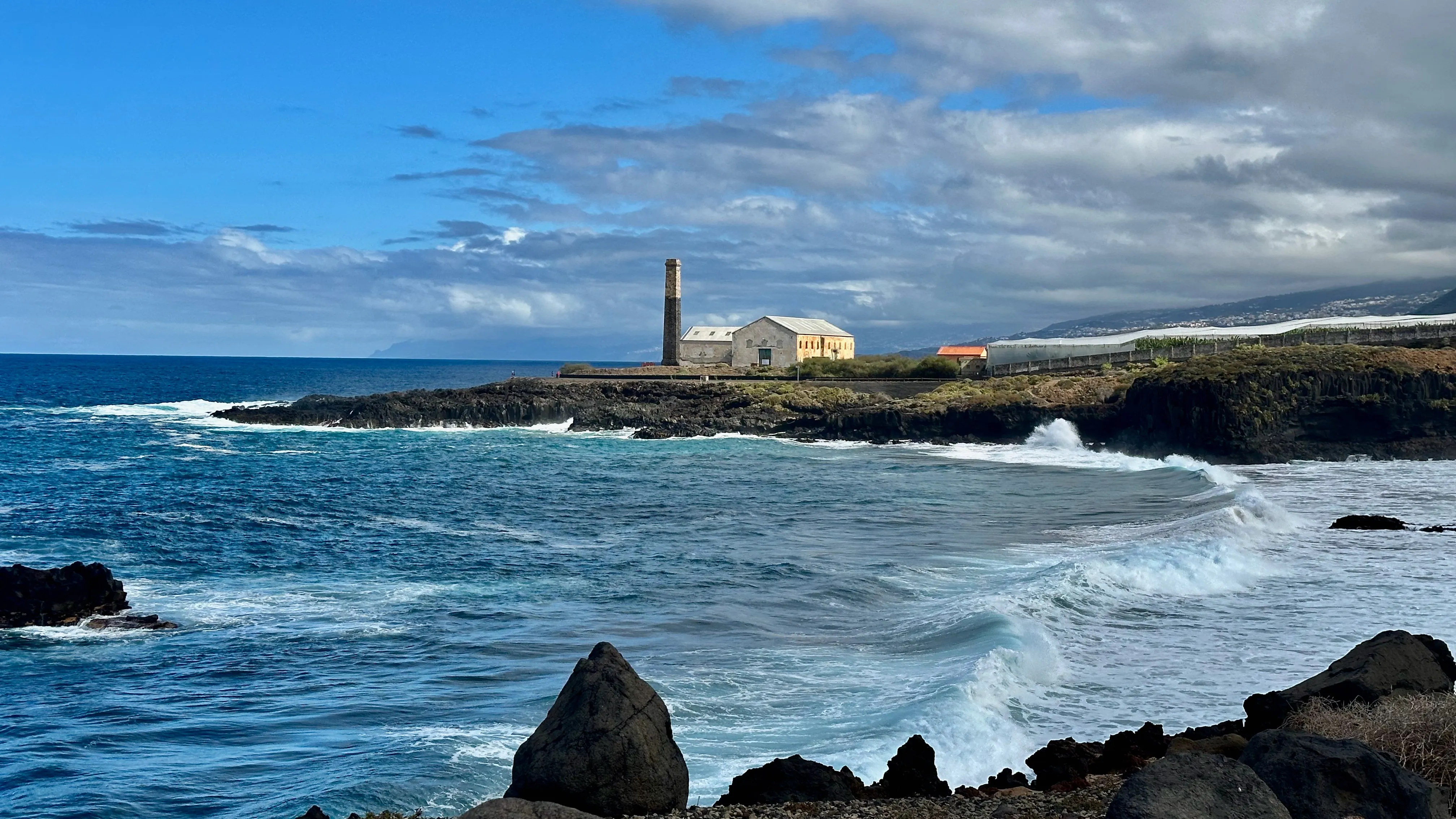 Stara fabryka z wysokim kominem stojąca na skalistym cyplu, obmywana falami oceanu na północnym wybrzeżu Teneryfy.