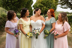 Bride standing with bridesmaids in pastel dresses, all holding bouquets in a garden setting.