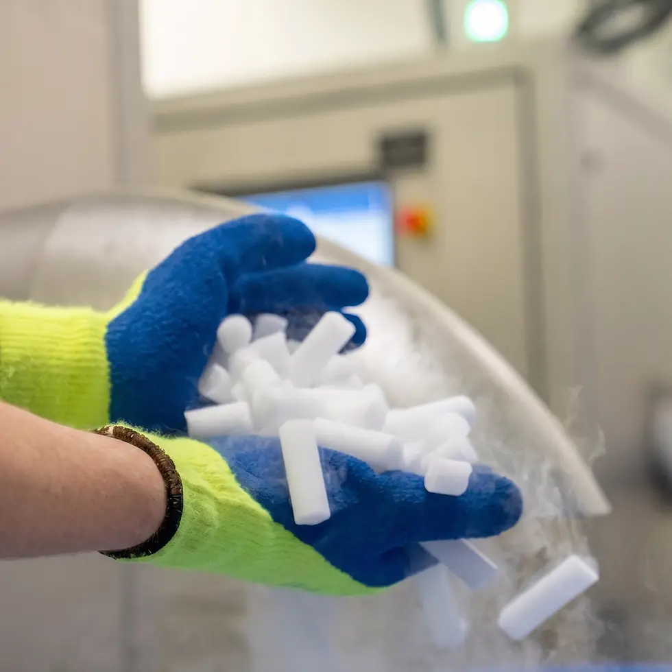 Zwei Hände in blau-gelben Schutzhandschuhen halten eine Handvoll zylinderförmiger, dampfender Trockeneis-Pellets.