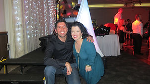 A man in a black shirt and a woman in a teal dress smile at the camera in a festive, indoor setting with colorful lights, decorations, and rave-worthy vibes perfect for DJ hire Melbourne, as seen in top event DJ testimonials.