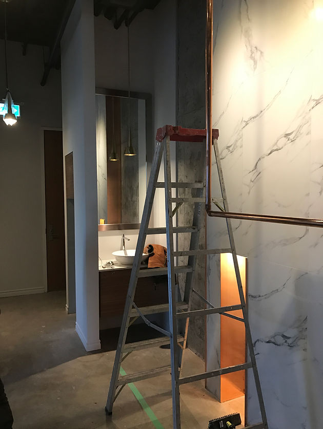 Z Square Group. The image depicts a large, open room with a concrete floor and white walls. There are two wooden shelves placed on the floor, one of which is empty, while the other is filled with various items such as books, bottles, and other objects. The room also features a large window with a view of the outdoors.