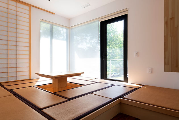 Toronto custom home design build project by Nestwood Home, Powered by Z Square  Group. The image depicts a spacious room with a tatami mat floor, a wooden table, and a sliding glass door leading to an outdoor area. The room is well-lit with natural light coming through the glass door and windows. The wooden table is placed in the center of the room, and there is a tatami mat sitting area in front of it. The tatami mat floor adds a traditional and cozy touch to the room, while the wooden table and sliding glass door create a sense of openness and connection to the outdoors. The overall atmosphere of the room is serene and inviting, making it an ideal space for relaxation and contemplation.