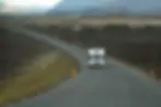 Una caravana blanca recorriendo una carretera solitaria en el paisaje volcánico de Islandia, con montañas en el fondo y un cielo nublado. La imagen captura la sensación de aventura y exploración en un entorno natural impresionante.