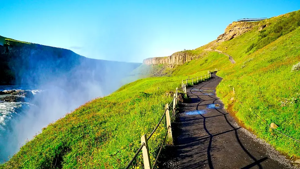 Scenic pathway along the Golden Circle in Iceland, with lush green hills and mist rising from a powerful waterfall