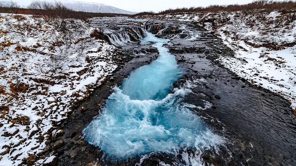Cascada Bruarfoss en invierno rodeada de nieve, con agua azul corriendo por la roca.