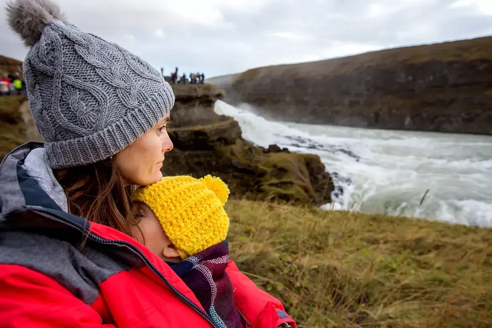Madre e hijo con ropa abrigada mirando una cascada en Islandia