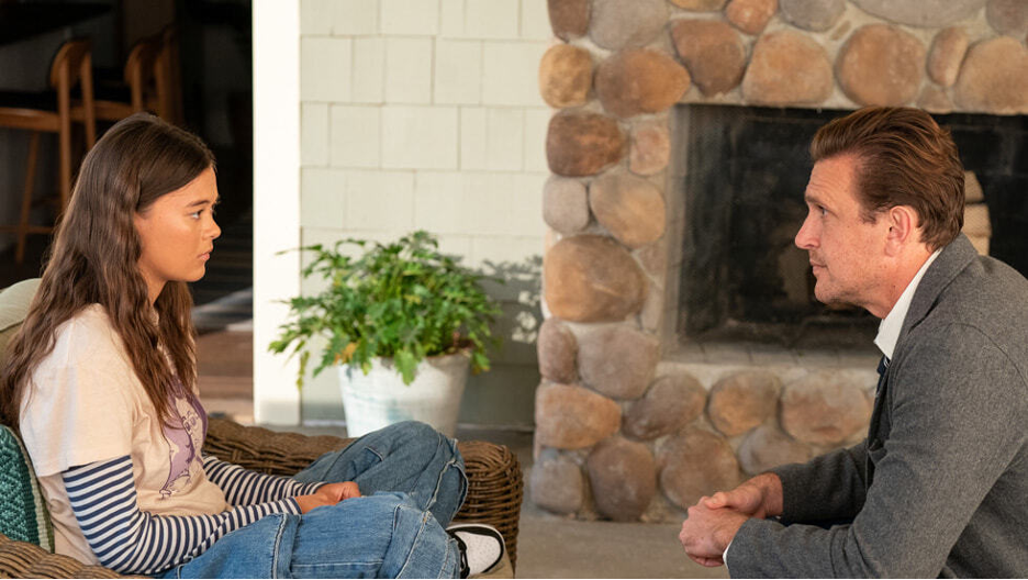 Young woman and man sit facing each other in a living room by a stone fireplace, appearing to talk seriously. Shrinking TV Show