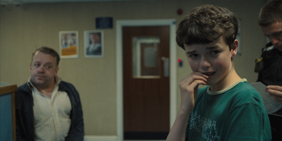 Thirteen-year-old Jamie Miller looks frightened while police officers stand beside him in an official still from Adolescence