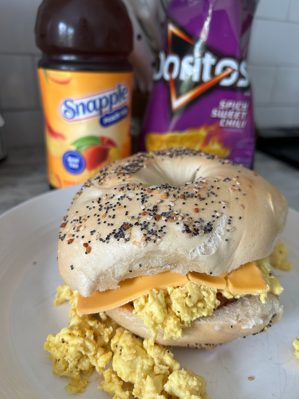 Another view of the bagel with egg and cheese on a white plate with the chips and iced tea