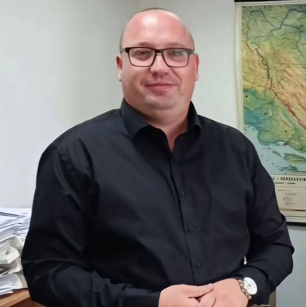 Portrait photo of a person in a black shirt standing in an office with a map on the wall