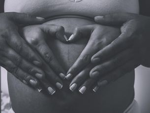 Ventre femme enceinte avec les mains du couple posées dessus formant un coeur