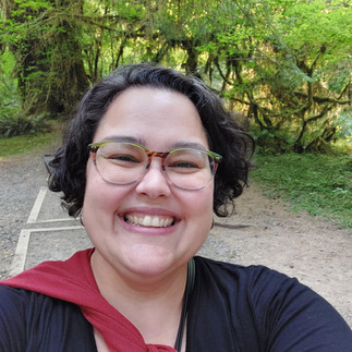 Picture of person with dark hair, glasses, smiling, black t-shirt and red jacket tied around the neck.