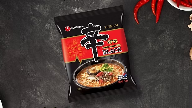 Shin Ramyun Black package displayed on a dark background with red chilies and garlic around it.