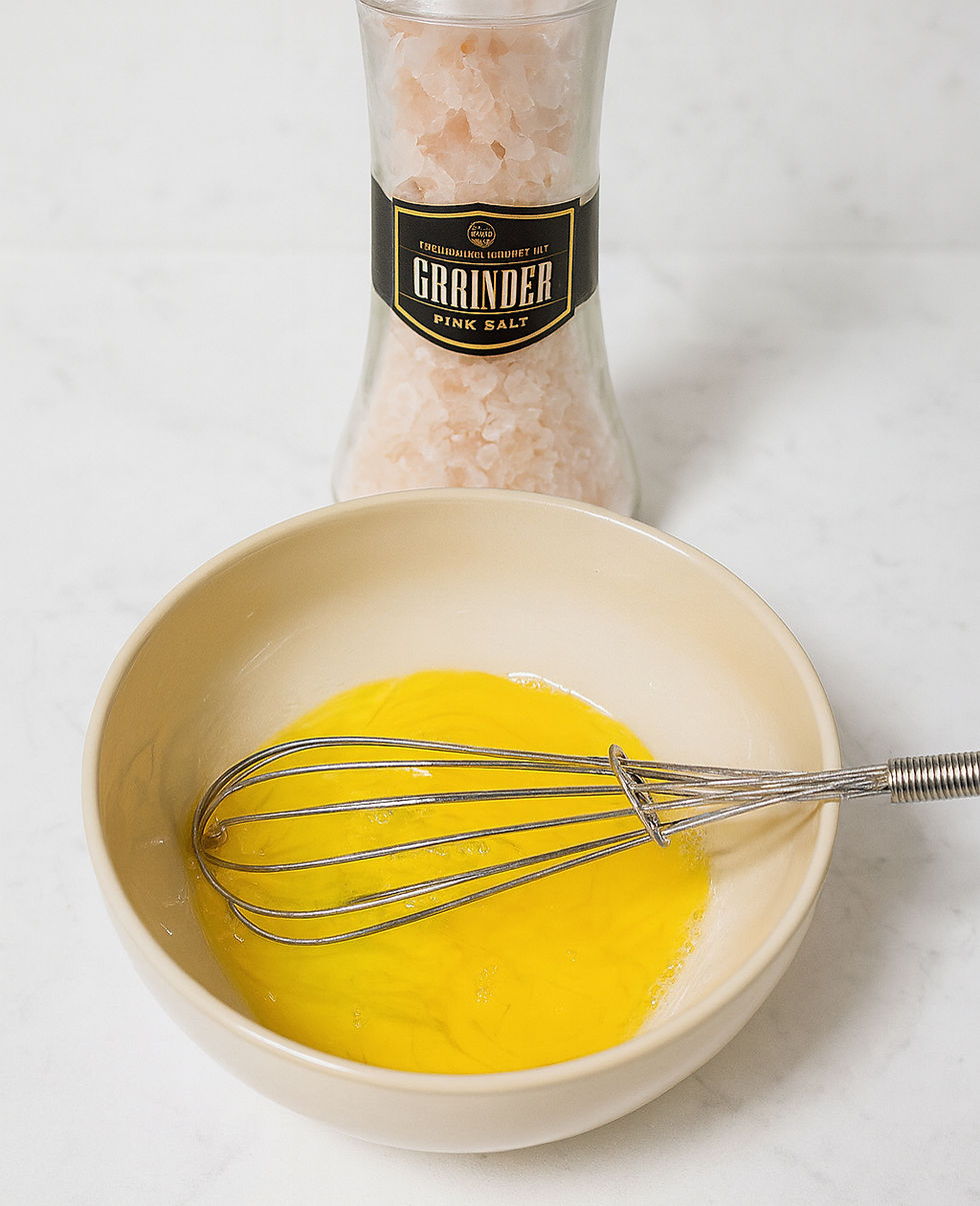 Beaten eggs: Bowl of whisked eggs with a metal whisk; pink salt grinder in the background.
