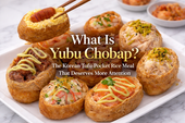 Premium blog thumbnail featuring assorted yubu chobap on a white plate over a white marble table, with colorful tofu-pocket rice pieces topped with beef, salmon, crab salad, and tuna beneath the title “What Is Yubu Chobap?”