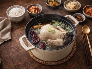Korean samgyetang served in a pot on a wooden table with rice and Korean side dishes (banchan) for a complete meal