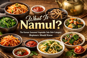 A premium blog thumbnail featuring assorted Korean namul side dishes in ceramic bowls on a rustic wooden table, with bold text reading “What Is Namul?” and smaller text describing it as a Korean seasoned vegetable side dish category beginners should know.