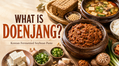 Wide commercial food thumbnail titled “What Is Doenjang?” featuring a large rustic bowl of chunky brown Korean fermented soybean paste on a warm cream tabletop. Around it are relevant doenjang ingredients and dishes, including soybeans, tofu, scallions, garlic, mushrooms, rice, kimchi, and a bowl of doenjang soup. The design has bright morning lighting, earthy Korean food styling, and a clean premium blog-thumbnail look.