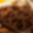 Ultra-macro close-up of glossy black-brown jajang ramen noodles coated in thick sauce. The image emphasizes the chewy curly noodle texture, shiny sauce cling, tiny seasoning specks, sesame seeds, and soft blurred toppings in the background.