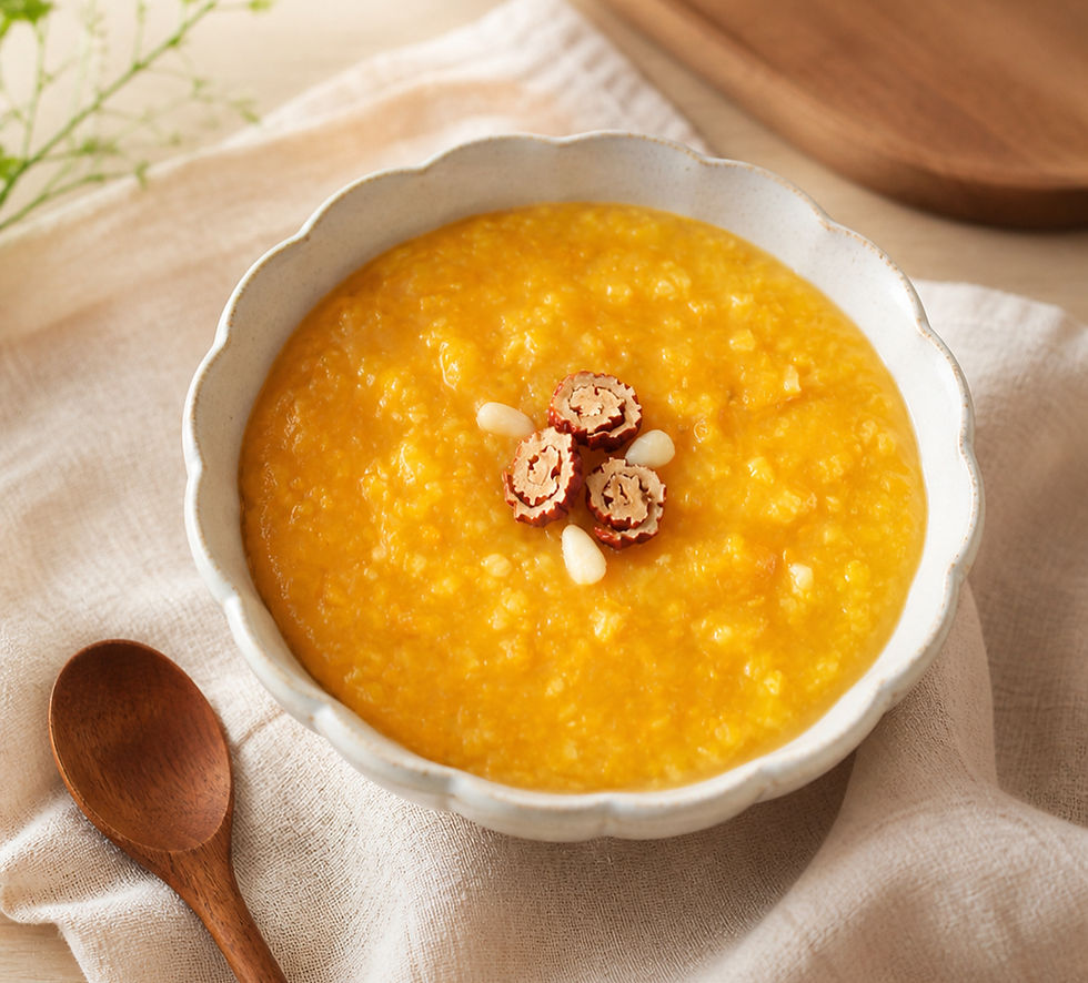 Bowl of golden Korean pumpkin porridge topped with jujube slices and pine nuts, served with a wooden spoon on soft beige linen.