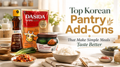 Bright Korean pantry add-ons blog thumbnail with sesame oil, beef stock powder, sliced napa cabbage kimchi, rice, gochujang, roasted seaweed, sesame seeds, scallions, and bold title text about pantry items that make simple meals taste better.