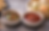 Landscape food image showing two Korean dumpling dipping sauces side by side on a stone tabletop, with crispy pan-fried mandu in a skillet, steamed dumplings in a bamboo basket, garlic cloves, red chilies, and scattered sesame seeds around them.