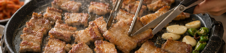 Bite-size pork belly pieces being cut and crisped with kitchen scissors and tongs beside garlic and green chilies.