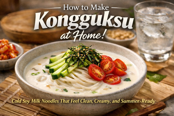 Creamy kongguksu in a beige bowl with cold soy milk broth, noodles, cucumber, seaweed, cherry tomatoes, and sesame seeds on a warm wooden table, with kimchi and iced water in the background and bold blog title text above.