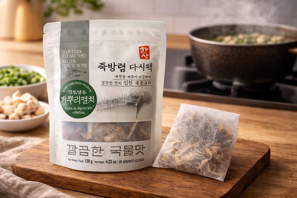 Hansang Radish & Anchovy Soup Stock (Tea Bag Type) pouch and tea bag displayed on a wooden cutting board in a warm kitchen setting, with broth ingredients and a steaming pot softly blurred in the background.