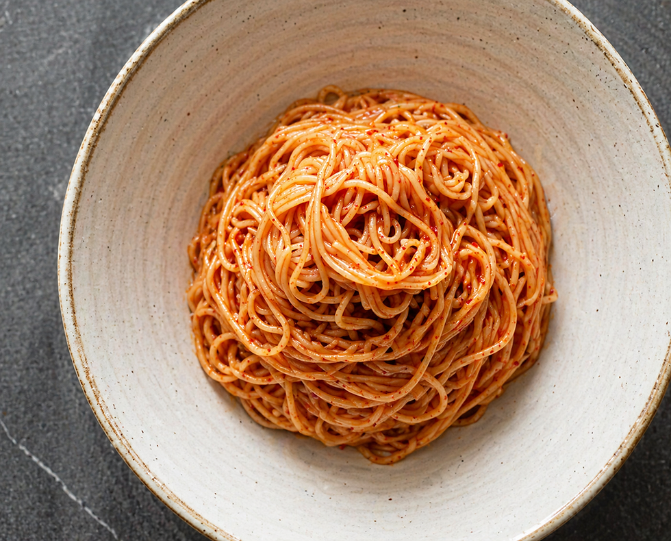 Bibim guksu noodles lightly coated in red spicy sauce, served as a simple mound in a wide ceramic bowl on a dark stone surface.