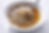 A white bowl of cold buckwheat noodles in light brown broth sits on a white marble surface, with a metal spoon resting at the rim in a close-up overhead photo.