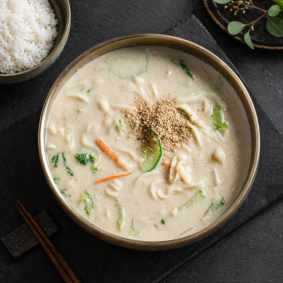 Top-down view of a bowl of creamy Korean perilla seed noodle soup topped with ground deulkkae, served on a dark slate background with a side bowl of white rice and chopsticks.