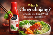 Blog thumbnail for What Is Chogochujang? featuring a red bottle of Korean chogochujang sauce beside a fresh mixed salad bowl topped with glossy red sauce, with bold title text on a warm dark background.