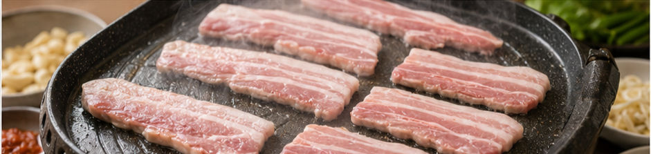 Raw pork belly slices laid in a single layer on a hot grill pan with steam rising.