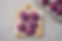 Top-down view of five purple sweet potato bread rolls on parchment paper over a wooden board, with more rolls on a tray in the corner